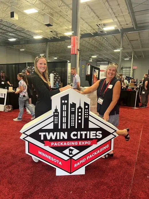 two people posing with a large foam prop in the shape of the TCP logo