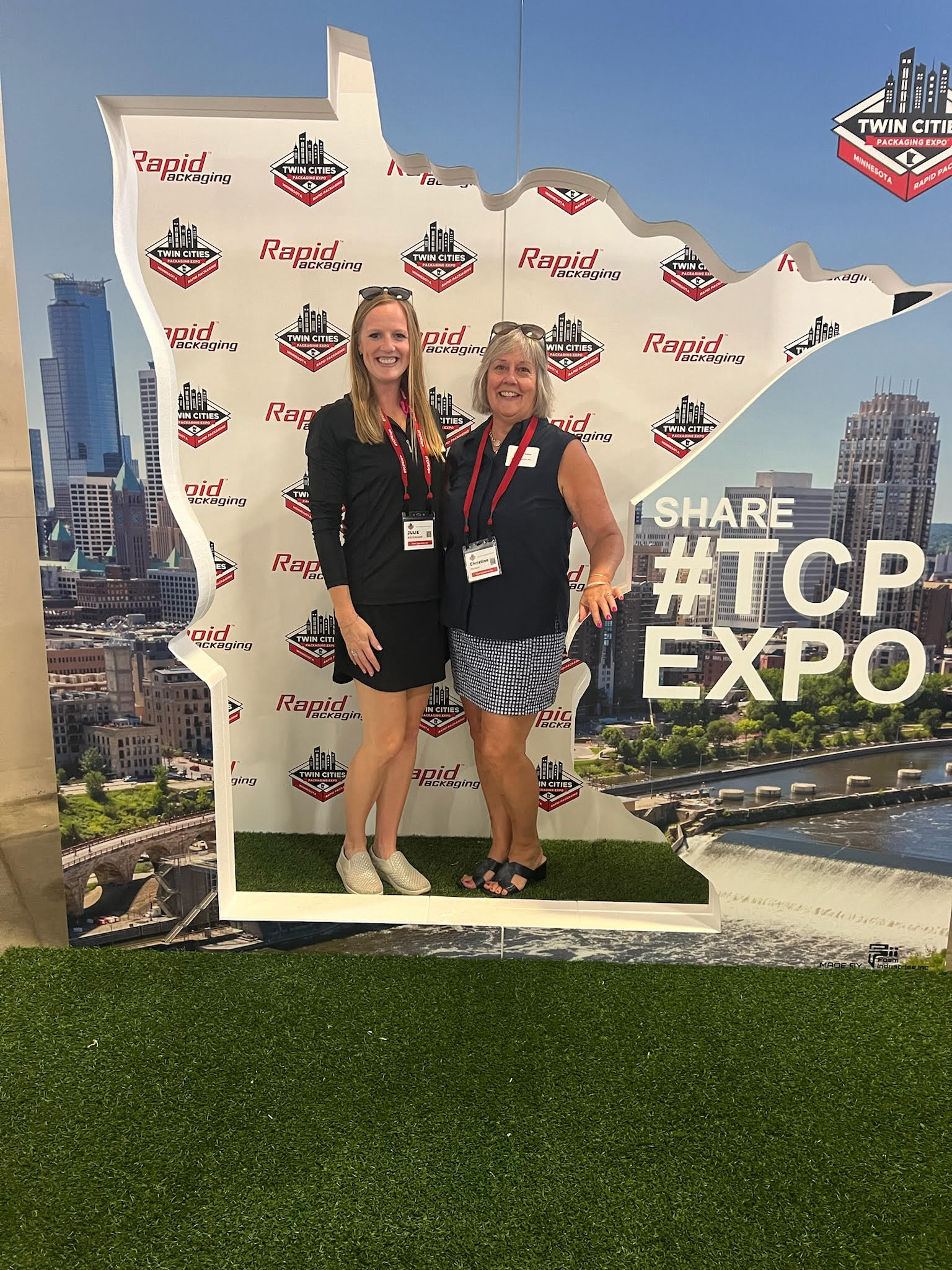 two people posing inside of a giant foam prop cutout of the state of MN at TCP Expo